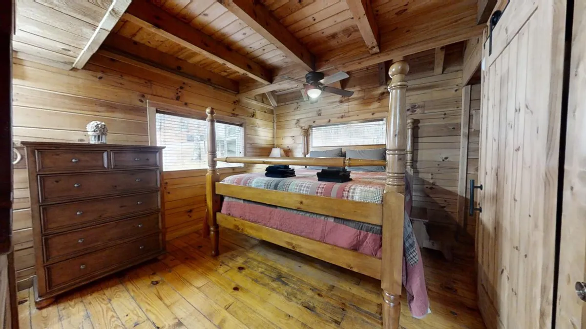 A peaceful master suite with a wooden bed and dresser, bathed in natural light from the windows. The serene setting highlights opportunities for relaxation and connection, with views of the surrounding landscape enhancing the sense of escape.