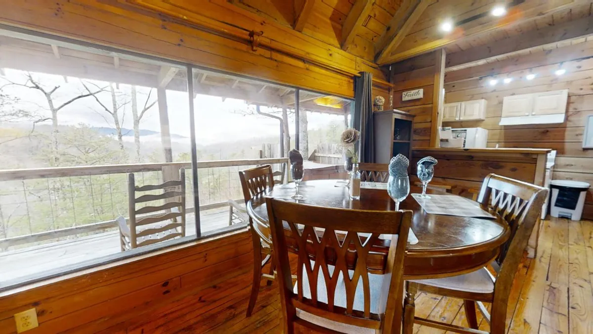 This shot showcases the dining table placed near expansive windows, wooden beams overhead, and the adjacent kitchen area. The natural light enhances the cozy, welcoming mood, while the layout encourages group gatherings and shared meals with scenic sunset views.