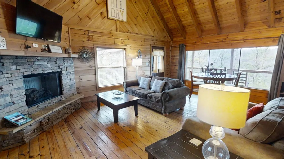 The photo spotlights a stone fireplace as the focal point, with a plush sofa and a dining area positioned near large windows that offer glimpses of the surrounding landscape. The space feels warm and welcoming, ideal for both relaxing and sharing meals with a view.