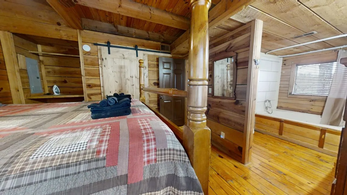 A welcoming queen bedroom with a wooden bed frame, plaid bedding, neatly arranged towels, and wooden walls that exude warmth. The space feels peaceful and private—ideal for couples or friends seeking their own retreat.