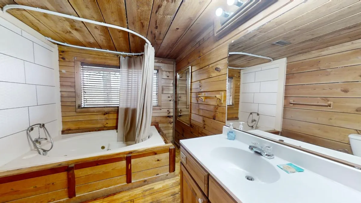 A bathroom with a wooden bathtub, vanity sink, and mirror, surrounded by rustic wood paneling. The space feels spa-like, emphasizing relaxation and rejuvenation after a long day.