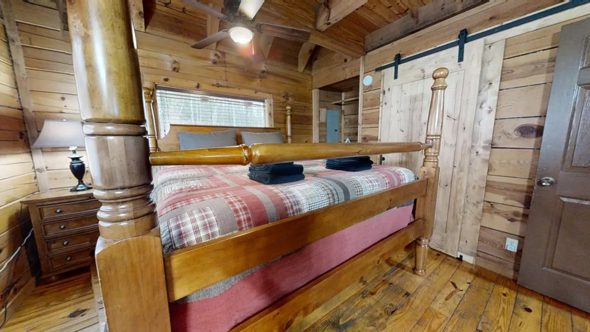 A cozy king bedroom with a four-poster bed, warm plaid bedding, wooden walls, wooden furniture, and a ceiling fan overhead. Soft lighting and rustic décor create an inviting atmosphere, perfect for relaxation after a day of adventure.