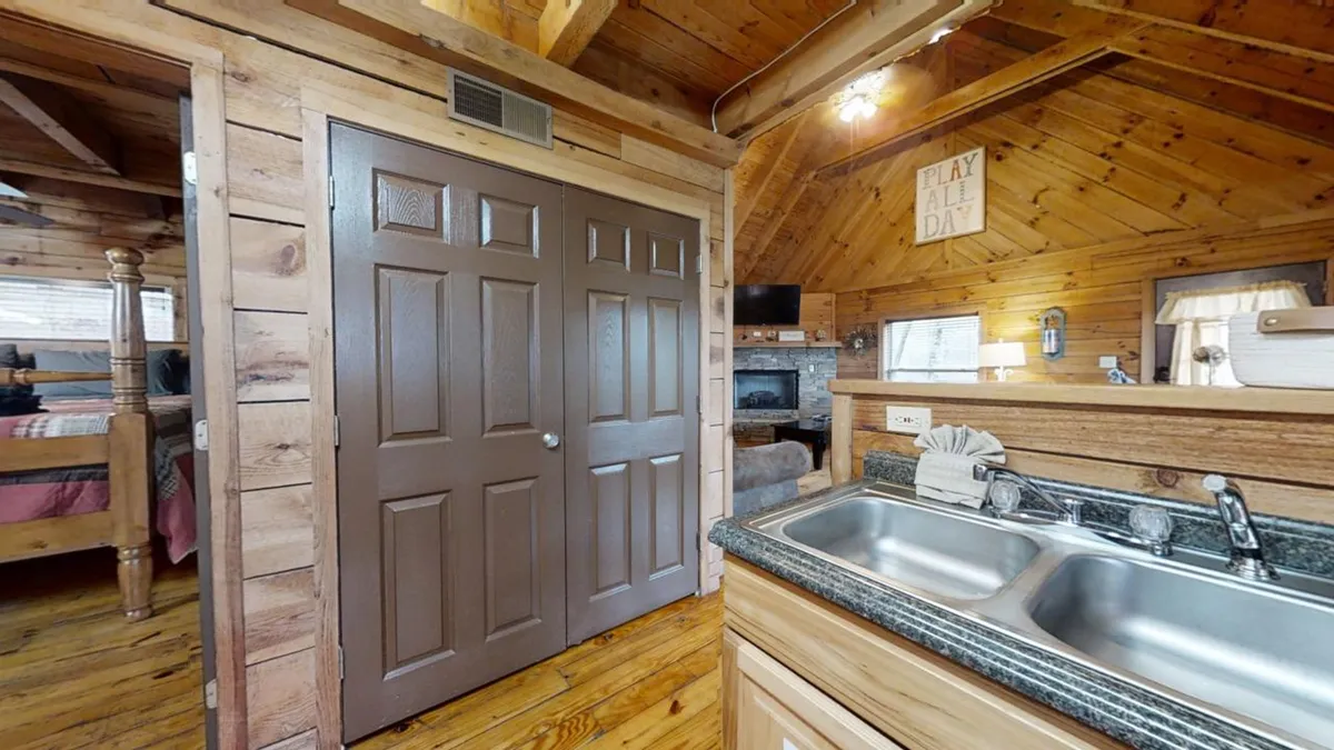 An open interior view featuring wooden doors, a kitchen sink, rustic beams, and homey wall decor. The space radiates warmth and is clearly designed for comfort—ideal for shared activities like game nights, relaxing after exploring, or enjoying a cozy meal together.