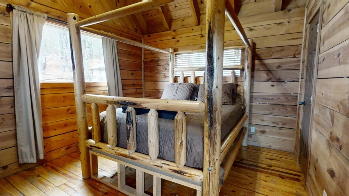 A bedroom with a log bed, wooden walls, and large windows that let in natural light, creating a restful and welcoming atmosphere. This space is perfect for unwinding after a day of adventure and reflects both tranquility and comfort.