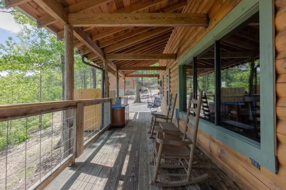 This image features an inviting porch scene with classic wooden rocking chairs and sturdy railings, set against a lush natural backdrop. Large windows reflect the sky, while the surrounding trees give a sense of tranquility and immersion in nature.